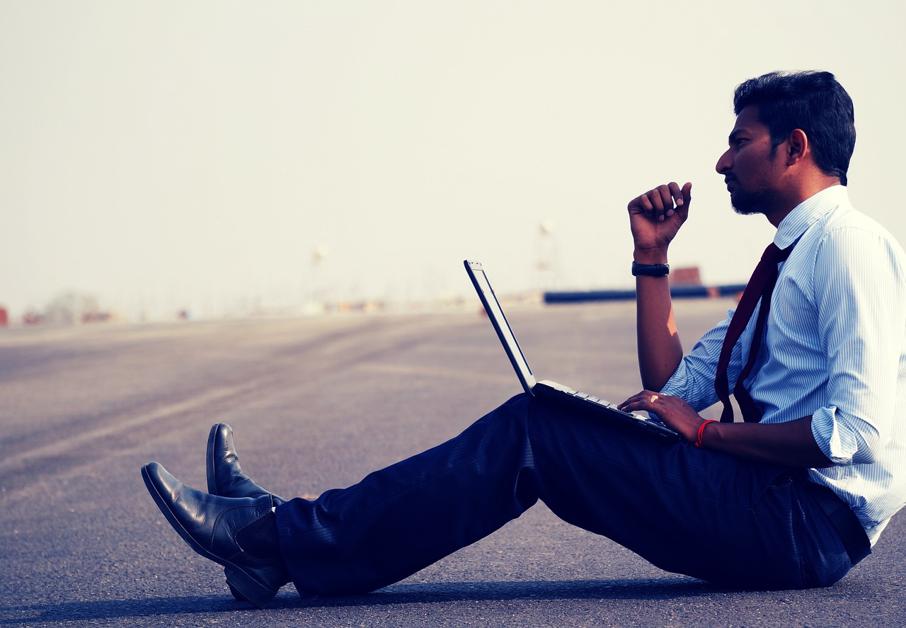 Man sitting on road with open laptop in his lap
